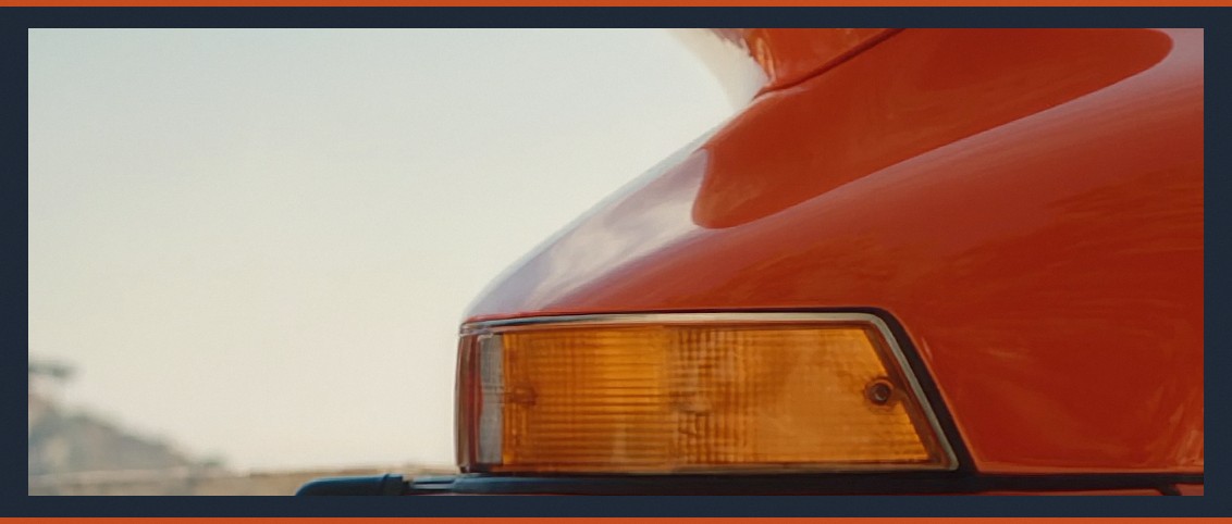 The star of @Image 2 — signal orange over deep-blue sea, chrome trim, whale tail. One car, by contract.