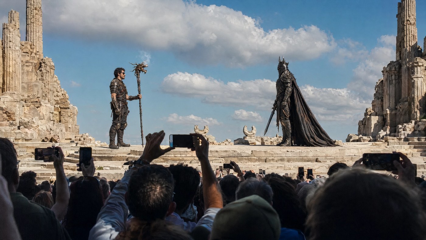 The staredown — hero stage-left, warlord stage-right, shot from mid-crowd with phones raised.