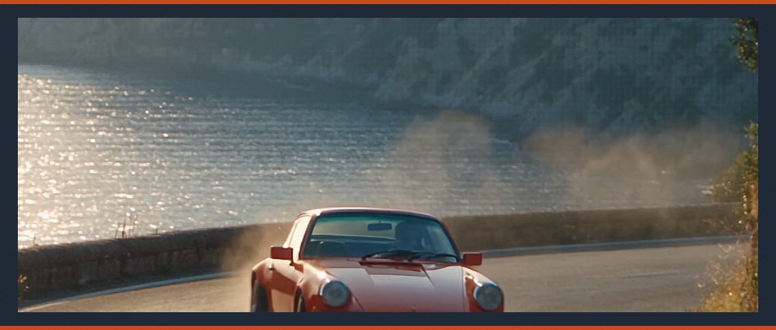 Shot 12 — the hairpin, sea far below, dust trailing. Static camera, moving subject: the cheapest luxury shot in cinema.