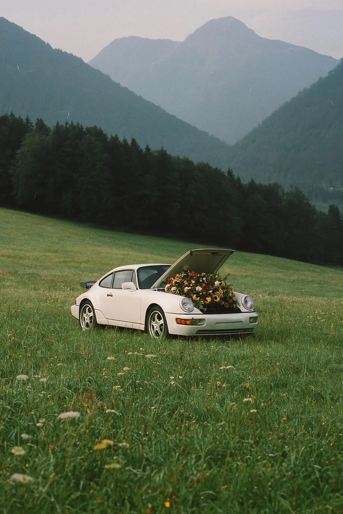 @Image 3 — the hero prop: one white classic coupe, a front trunk overflowing with wildflowers, tall meadow — and the 35mm grain the whole film is graded to.